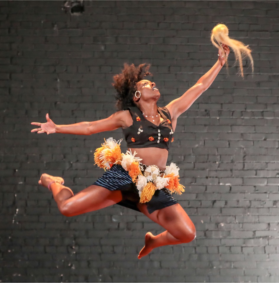Quianna Simpson airborne with arms extended and knees bent against a brick backdrop