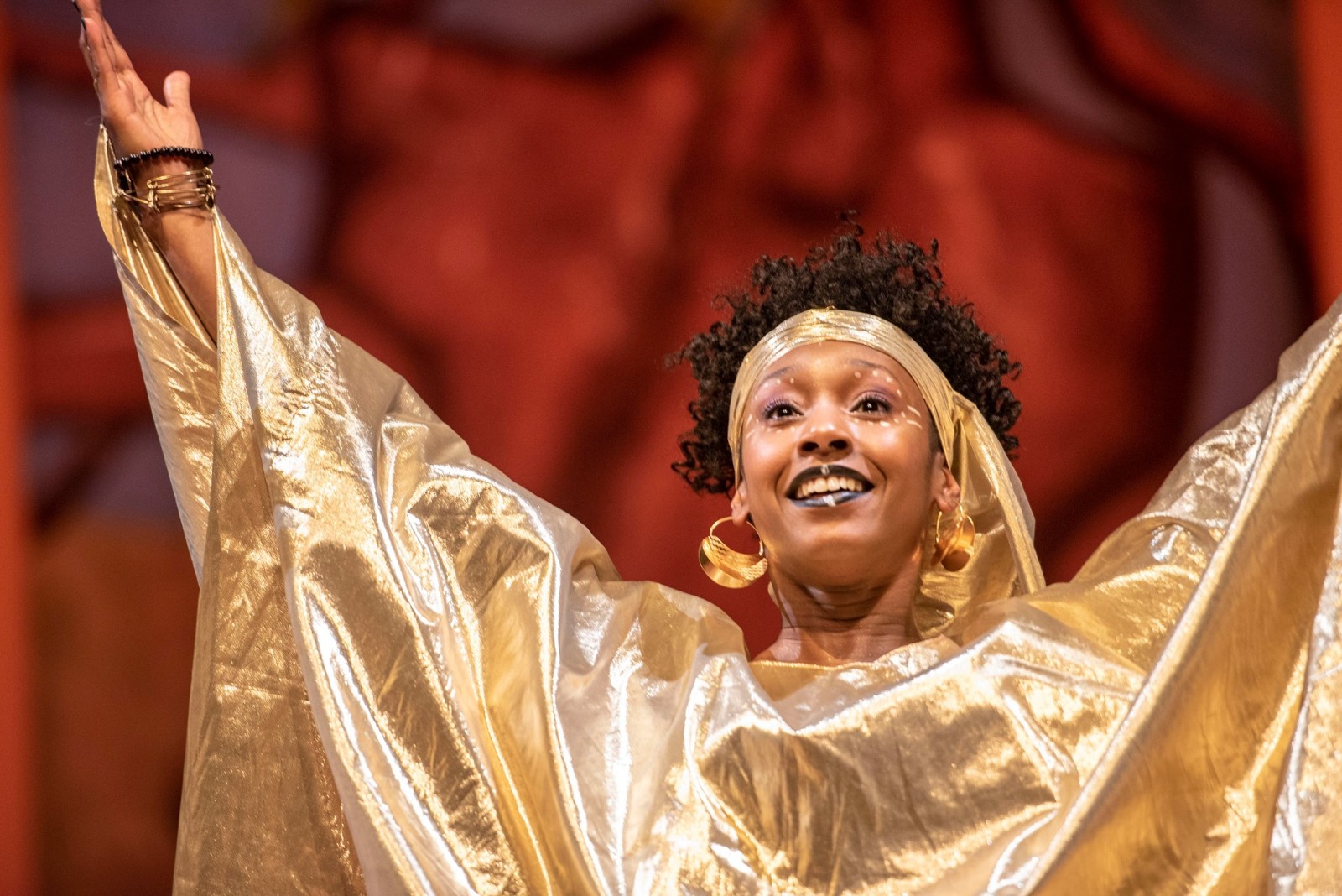 Quianna Simpson in a gold costume, smiling upward with both arms raised